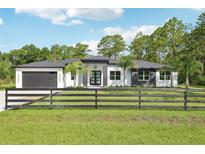 Contemporary home featuring a dark gray garage door and a well-manicured front yard with a wooden fence at 42157 Tamarac St, Eustis, FL 32736