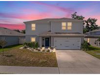 Two-story home featuring a gray exterior, two-car garage, and a manicured lawn at 253 Fiddlewood Ct, Davenport, FL 33837
