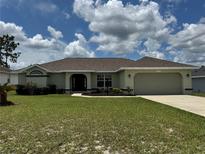Charming one-story home with a well-manicured lawn and attached two-car garage on a sunny day at 8414 Sw 136Th Pl, Ocala, FL 34473