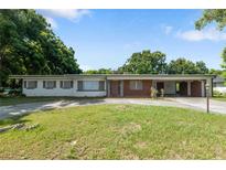 Ranch-style home featuring a brick facade, long driveway, covered parking, and mature trees against a blue sky at 622 Avenue D Se, Winter Haven, FL 33880