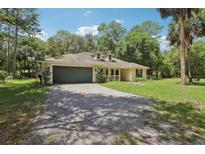 Inviting single-story home featuring a two-car garage and a gravel driveway surrounded by a lush green lawn at 15888 Ne 152Nd Ave, Fort Mc Coy, FL 32134