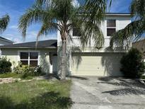 Two-story home featuring a two-car garage, a front door, and tropical landscaping with palm trees at 1909 Lakeview Pl, Kissimmee, FL 34759