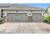 Attached two car garage doors with stone accents and brick paved driveway at 31980 Geoff Way, Sorrento, FL 32776