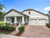 Charming one-story home featuring a two-car garage, brick driveway, covered front porch with stone-clad columns, and manicured landscaping at 8030 John Hancock Dr, Winter Garden, FL 34787