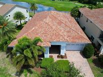 Charming home with a red tile roof, lush landscaping, and a view of the community lake and golf course at 9979 Winnington St, Orlando, FL 32832