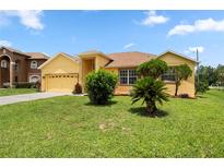 Charming yellow home featuring a lush green lawn, landscaped front yard, and two-car garage at 1457 Teal Dr, Kissimmee, FL 34759