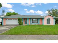 Charming single-story home with a well-maintained lawn and attached garage, features a whimsical pink and teal exterior at 2309 Cilantro Dr, Orlando, FL 32837