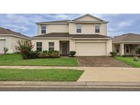 Two-story home featuring a paver driveway, lush landscaping, and a well-manicured lawn at 565 Ogelthorpe Dr, Davenport, FL 33897