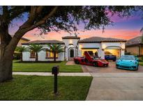 Stunning home at dusk boasts lush lawn, tile roof, and multiple luxury cars in the driveway and garage at 7733 Pointe Venezia Dr, Orlando, FL 32836