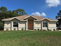 Charming single-story home with a well-maintained lawn, neat flowerbeds, and an inviting coral colored front door at 56 Redwood Rd, Ocala, FL 34472