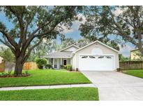Charming single-story home featuring a well-manicured lawn, mature trees, and a two-car garage at 1052 Royal Oaks Dr, Apopka, FL 32703