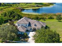Stunning aerial view of a grand home with a tile roof, mature trees, and a tranquil lake backdrop at 13025 Lake Roper Ct, Windermere, FL 34786
