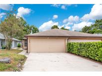 Tan-colored one-story home featuring a two-car garage, lush landscaping, and a concrete driveway at 378 Cedarbrook Ln, Altamonte Springs, FL 32714