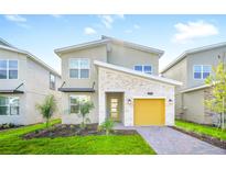 Charming two-story home with modern design, stone accents, landscaped yard and bright yellow garage door at 9175 Sommerset Hills Dr, Davenport, FL 33896