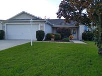Charming one-story home with a well-manicured lawn, mature tree, and attached garage at 1425 Hollyberry Pl, The Villages, FL 32162
