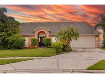 Inviting single-story home featuring a two-car garage, beautifully landscaped yard, and a striking pink exterior at sunset at 1606 Burryport Dr, Orlando, FL 32837