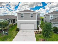 Two-story home featuring gray siding, a white two-car garage, and a well-maintained lawn at 7367 Catania Loop, Clermont, FL 34714