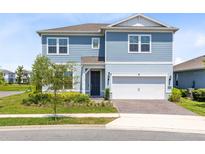 Two-story home featuring blue siding, a well-manicured lawn, and a two-car garage with a brick-paved driveway at 13829 Destin Beach Ln, Orlando, FL 32827