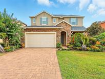 Charming two-story home featuring stone accents, a brick driveway, and lush landscaping under a blue sky at 16995 Tradewind Pt, Winter Garden, FL 34787