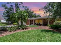 Charming brick home featuring lush landscaping and a cozy front porch seating area at 27 Fairway Dr, Eustis, FL 32726