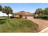 Inviting single-story home featuring a well-manicured lawn, mature palm trees, and a brick-paved driveway at 8463 Sw 84Th Loop, Ocala, FL 34481