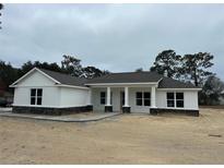 Single-story home with white siding, dark gray stone accents, and a covered porch at 5912 Ne 57Th N Loop, Silver Springs, FL 34488