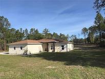 Charming single-story home featuring a well-manicured lawn and set amongst a backdrop of lush trees and a clear blue sky at 12205 Sw 71St Lane Rd, Ocala, FL 34481