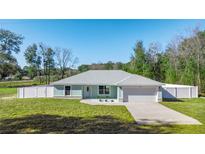 Newly built home with light teal exterior, white fence, and a two-car garage at 14462 Se 28Th Ct, Summerfield, FL 34491