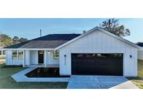 White farmhouse exterior with black garage door and landscaping at 8968 Se 156Th St, Summerfield, FL 34491