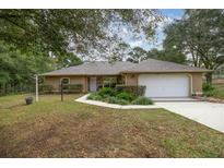 Tan one-story house with a white garage door and landscaped yard at 8465 Sw 202Nd Ter, Dunnellon, FL 34431