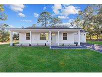 White house with a front porch, gray driveway, and a landscaped lawn at 15002 Sw 27 St, Ocala, FL 34481