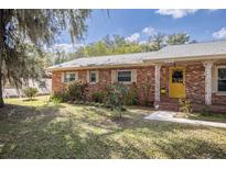 Charming brick home featuring a bright yellow front door and landscaped front yard with mature trees at 820 Ne 42Nd Ter, Ocala, FL 34470