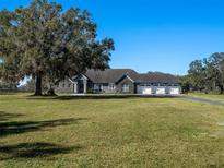 Gray house with stone accents, three-car garage, and large oak tree in front at 12330 Nw 35Th St, Ocala, FL 34482