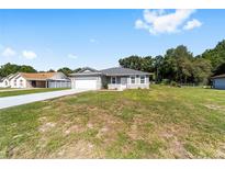 Charming single-story home with a well-manicured lawn and a two-car garage on a sunny day at 10871 Sw 62Nd Avenue Rd, Ocala, FL 34476