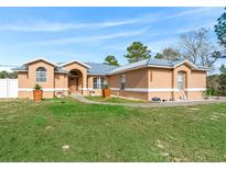 Tan house with gray metal roof, walkway, and landscaping at 22287 Sw Mango Ln, Dunnellon, FL 34431