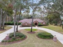 Brick home with circular driveway, lush landscaping, and mature trees at 7267 Se 12Th Cir, Ocala, FL 34480