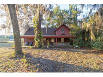 Rustic red house with covered porch sits on a grassy lot, surrounded by large trees at 876 Ne 71St Ln, Ocala, FL 34479