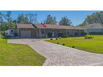 Brick home with paver driveway, mature landscaping, and American flag at 11418 Lake Eustis Dr, Leesburg, FL 34788