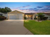 Tan one-story house with a two-car garage and well-maintained lawn at 17606 Se 93Rd Butler Ct, The Villages, FL 32162