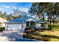 Single-story home with a white garage door and a brick driveway, surrounded by lush landscaping at 10801 Sw 71St Ave, Ocala, FL 34476