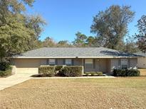 Beige house with gray roof, attached garage, and landscaping at 73 Fir Dr, Ocala, FL 34472