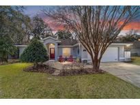 Charming single-story home featuring a well-maintained lawn, mature tree, and cozy red seating area at entrance at 2412 Se 23Rd Pl, Ocala, FL 34471