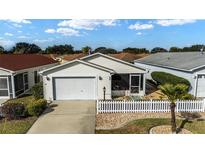 Charming single-story home with a two-car garage, screen porch, and a beautifully landscaped front yard and a white picket fence at 1112 Carvello Dr, The Villages, FL 32162