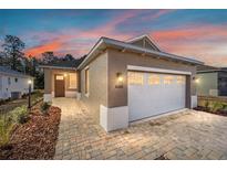 Charming exterior showcasing a manicured lawn and a two-car garage with a brick-paved driveway, under a vibrant twilight sky at 10306 Sw 99Th Ln, Ocala, FL 34481