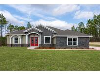 Charming single-story home featuring stone accents, a well-manicured lawn, and a striking red double-door entrance at 12217 Sw 67Th Ln, Ocala, FL 34481