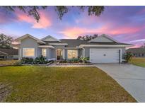 Gray house with white accents, two-car garage, and landscaped yard at 17470 Se 115Th Terrace Rd, Summerfield, FL 34491