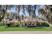 House exterior showcasing a tan house with a covered porch, green lawn, and mature trees at 12854 Se 118Th Ter, Ocklawaha, FL 32179