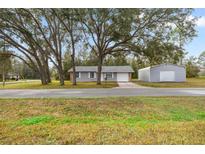 Charming single-story home featuring mature trees, gray stucco siding, and an attached one car garage at 26 Spring Cir, Ocala, FL 34472