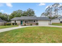 Charming home featuring a teal door, well-manicured lawn, and an attached two car garage at 6 Cherry Drive Ln, Ocala, FL 34472