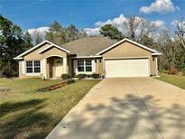 Charming single-story home featuring a two-car garage and a well-manicured lawn under a bright blue sky at 5765 Sw 164Th Pl, Ocala, FL 34473